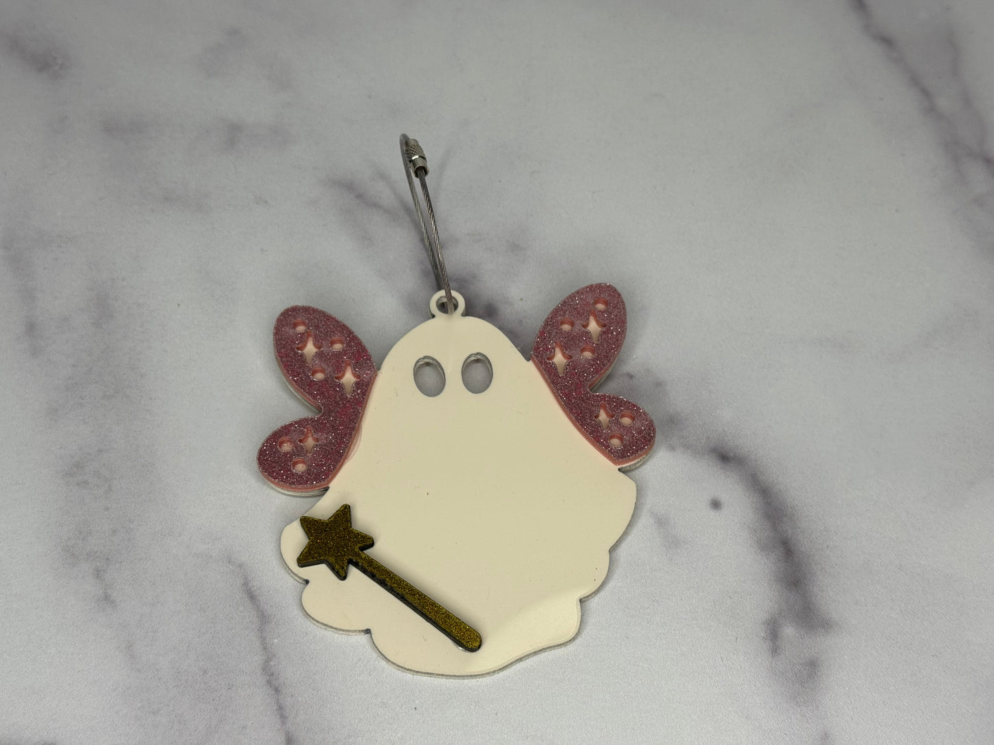Ghost-shaped keychain with a wand on a marble background