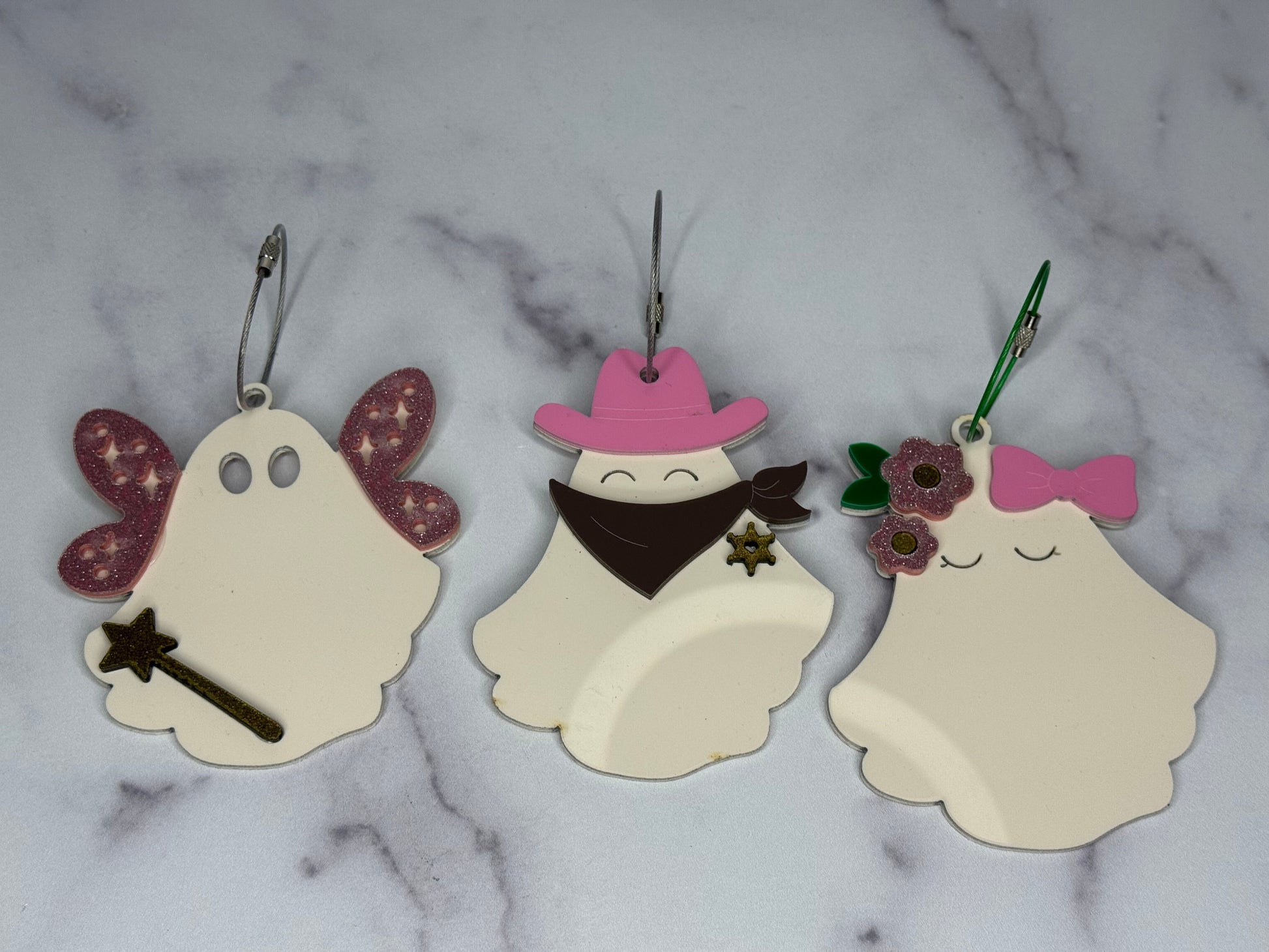 Three ghost-shaped keychains with decorative elements on a marble background