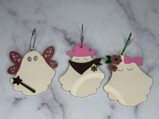 Three ghost-shaped keychains with decorative elements on a marble background